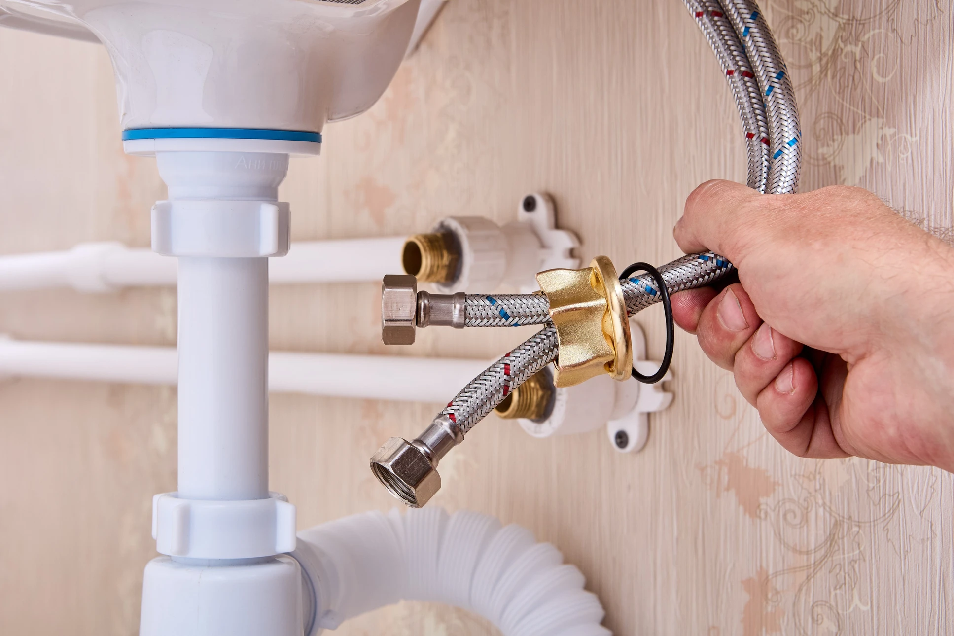 Plombier installant un flexible d'alimentation en eau sous un lavabo de salle de bain
