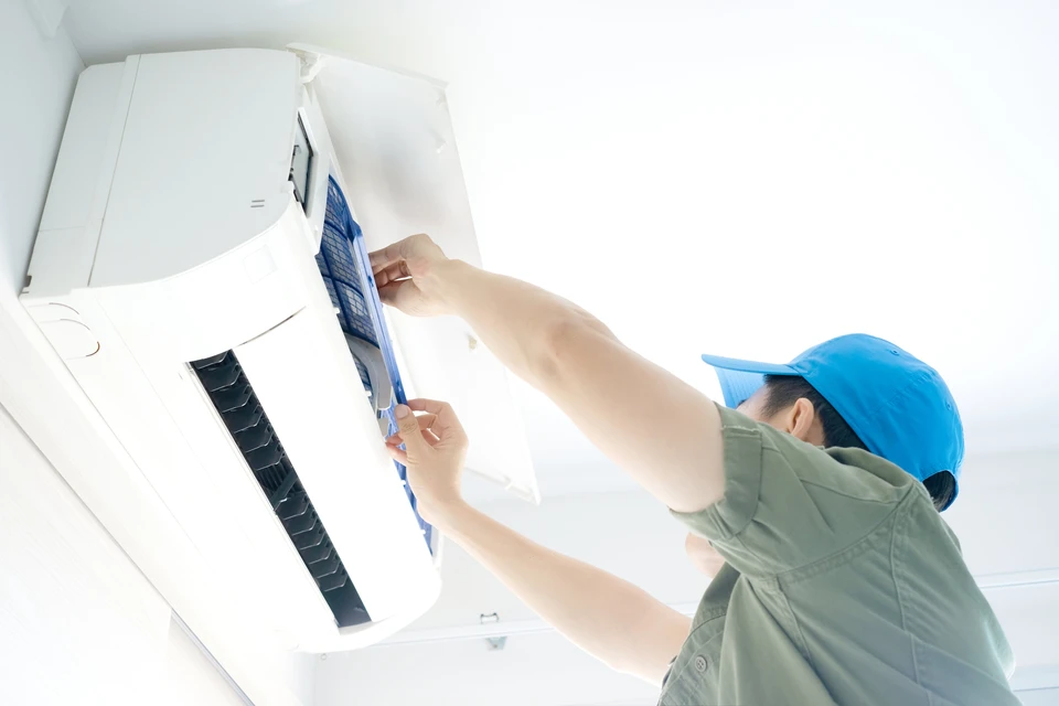 Technicien en uniforme bleu effectuant la maintenance d'un climatiseur mural split