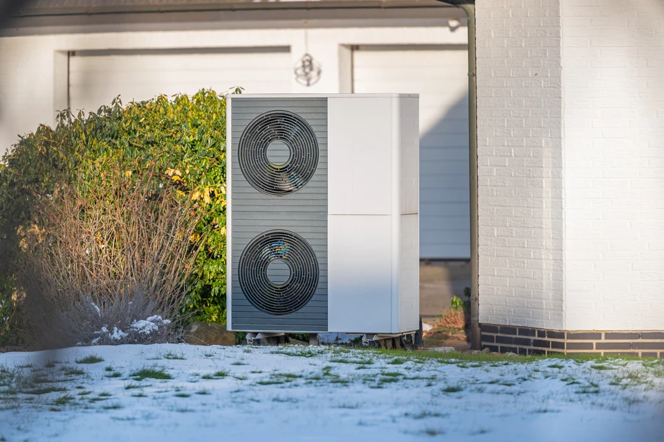 Placé près du mur d'un cottage moderne, l'unité extérieure d'une pompe à chaleur est visible